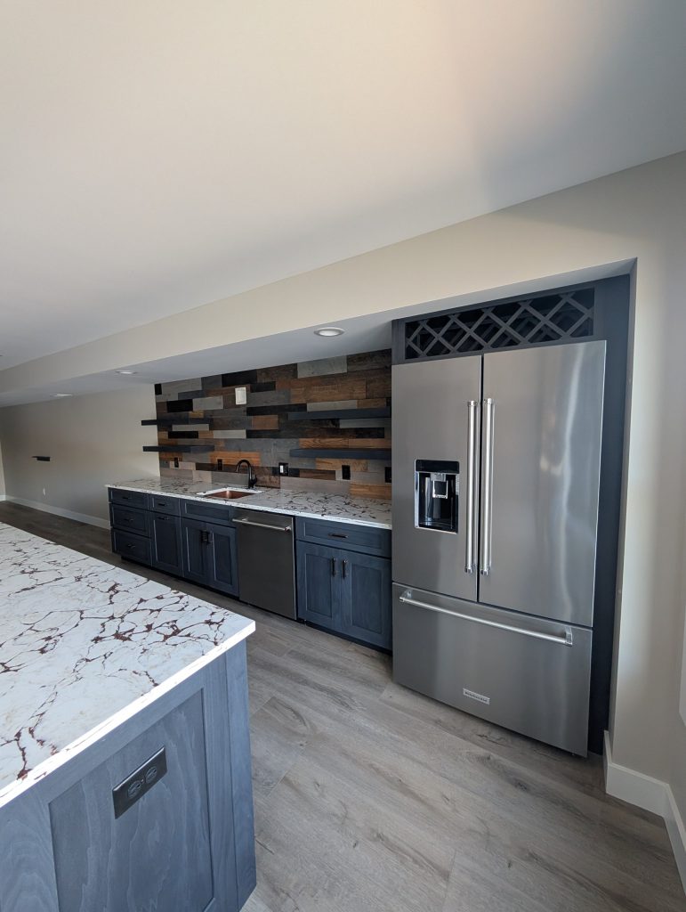 Lower-level wet bar with blue cabinets and a stainless refrigerator at The Lake House